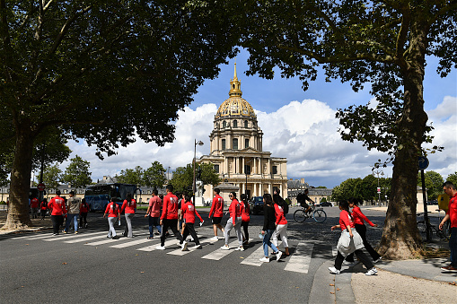 Paris, France-07 29 2023: Group of people crossing street in front of Les Invalides formally the Hôtel national des Invalides, which is a complex of buildings in the 7th arrondissement of Paris, France, containing museums and monuments, all relating to the military history of France, as well as a hospital and a retirement home for war veterans, the building's original purpose.