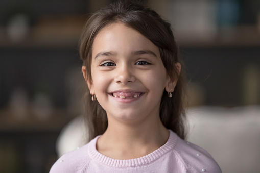 Happy pretty sweet preschool girl head shot portrait. Cheerful cute black haired kid posing at home, looking at camera with toothy gap smile, laughing, enjoying childhood. Video call screen