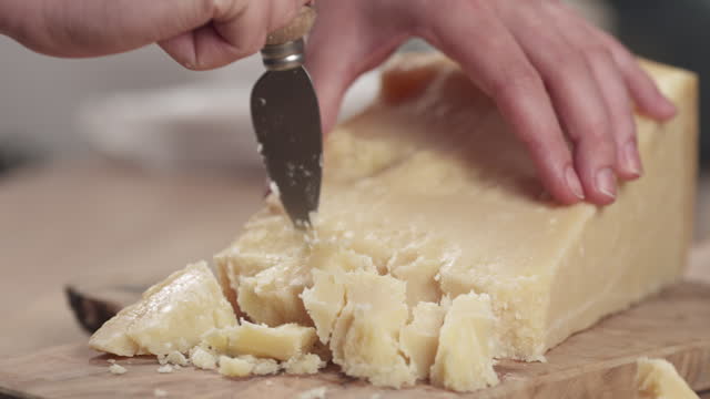 Slow motion slide of female hand cutting hard parmesan cheese