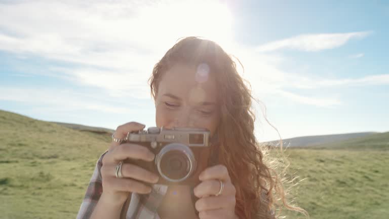 Beautiful young woman taking photo with retro styled digital camera at sunset Girl photographing with bright sunny sun flare light creativity concept