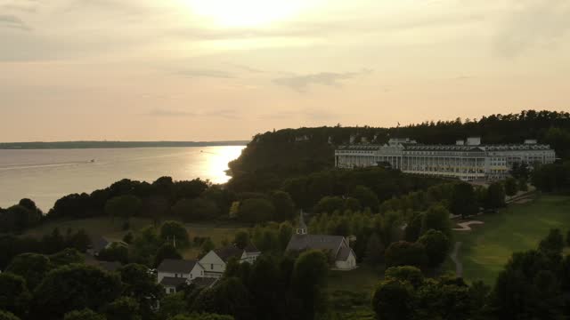 Drone shot over Grand hotel surrounded by green trees at Mackinac island during golden hour