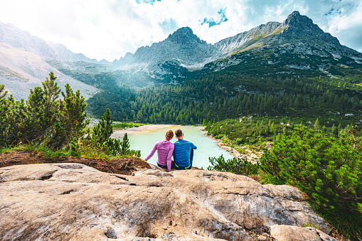 Description: Young sportive couple enjoys view on the turquoise Sorapis lake from a beautiful restpoint in the afternoon. Lake Sorapis, Dolomites, Belluno, Italy, Europe.