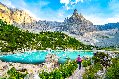 Description: Athletic woman enjoys beautiful walk at turquoise Sorapis lake with dito di dio in the background in the evening. Lake Sorapis, Dolomites, Belluno, Italy, Europe.