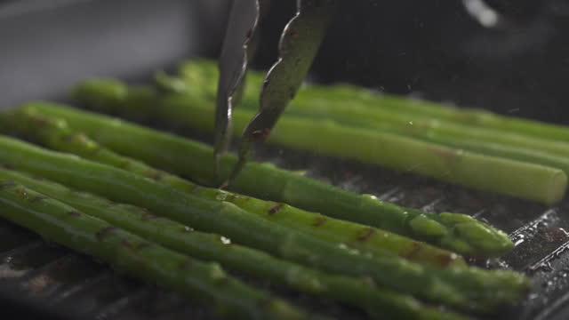 Slide slow motion shot of turning frozen green asparagus on grill pan