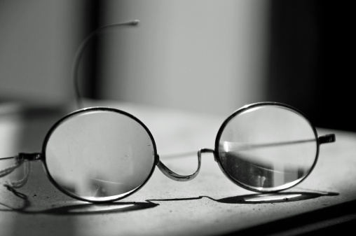 A pair of antique glasses on a desk that is lighted by sunlight. Black and white.