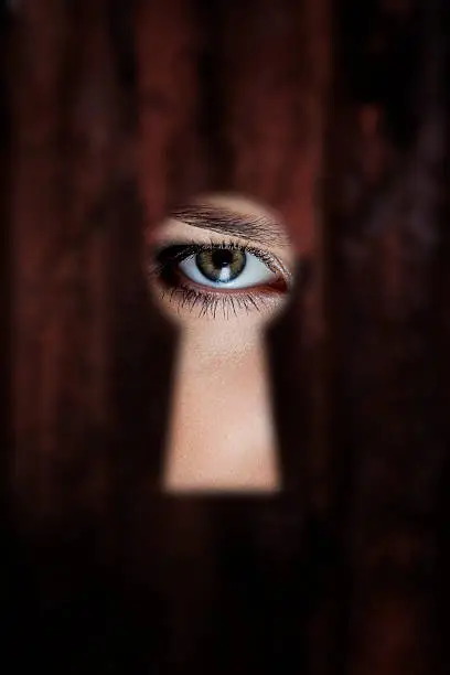 Female eye looking through a keyhole 