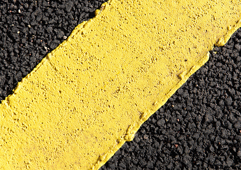 Macro image of a recently painted yellow line on fresh tarmac.