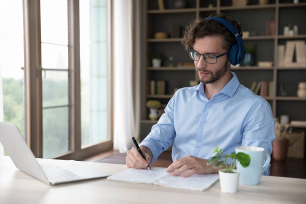 istock Serious young adult student man in wireless headset watching webinar 1579155272