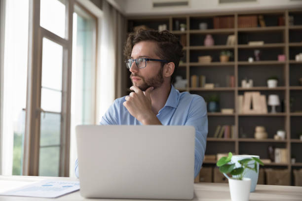 istock Serious young freelancer man in glasses thinking on business project 1579155277