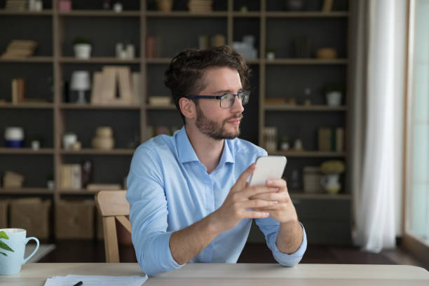 istock Thoughtful dreamy business man holding smartphone, sitting at work table 1579155789