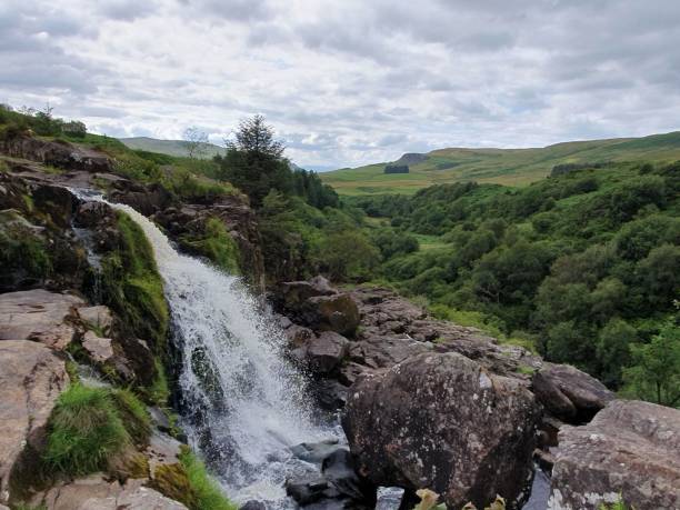 istock Crashing waterfall in green countryside with grey overcast sky 1579211350