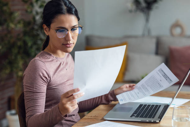 istock Beautiful young woman looking at papers while working with pc 1579213422