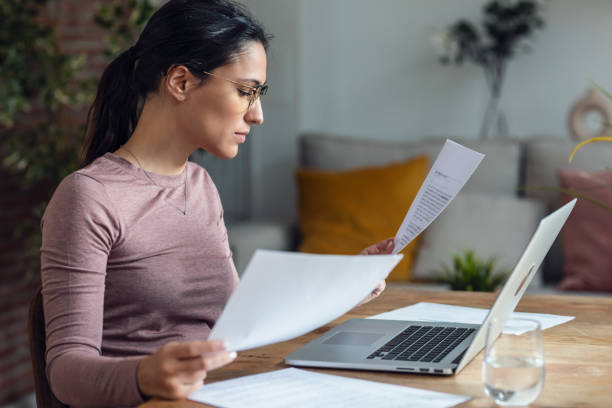 istock Beautiful young woman looking at papers while working with pc 1579213965