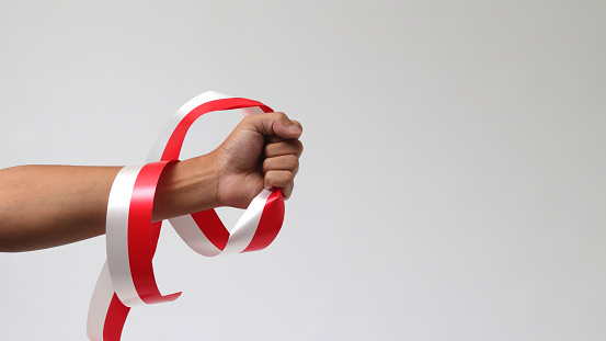 A man with a fist holding a red and white ribbon with empty copy space isolated on a white background, representing Indonesia Independence Day concept