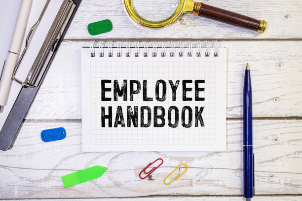 On a yellow background lies a pen and a black notebook with the inscription - Employee Handbook stock photo