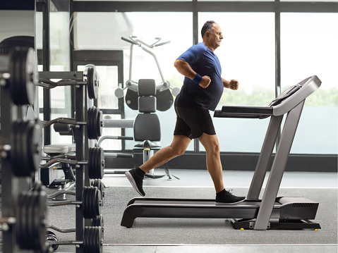 Full length profile shot of a mature man running on a treadmill at the gym