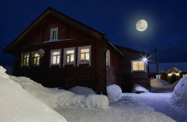 Electric light in windows of winter rural house on  moonlit night.