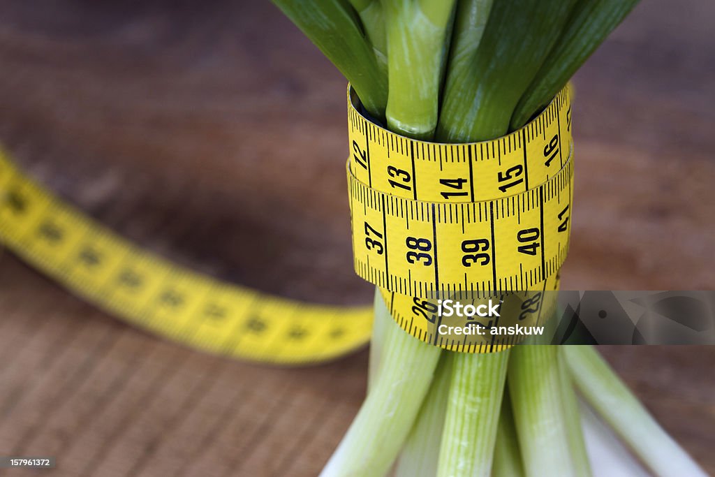 Green onions with yellow measurement tape Green onions with yellow measurement tape on rustic wooden background; weight loss and diet concept Close-up Stock Photo
