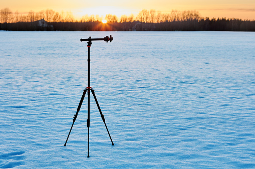 Golden hour for photography, lightweight aluminum tripod is mounted on snowy crust.