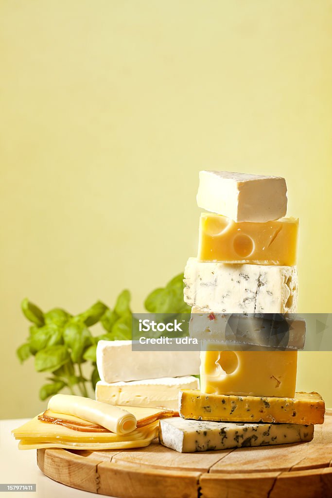 Pile of cheese many various types Pile of cheese many various types on cutting board against yellow background with basil Appetizer Stock Photo