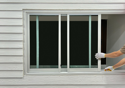 Construction worker repairing the sliding window on artificial woods siding.