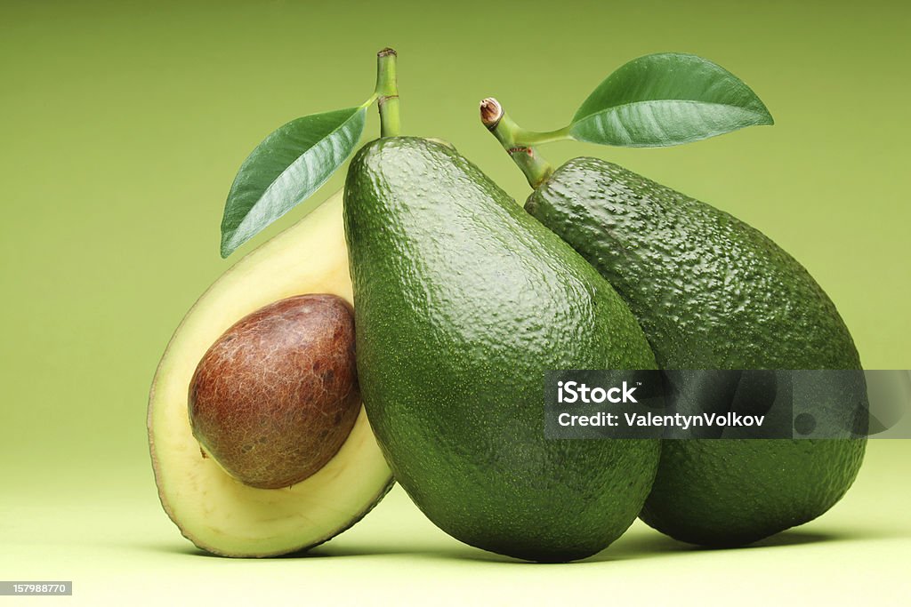 Three avocados with one sliced in half Avocado isolated on a green background. Avocado Stock Photo