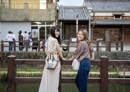 Happy young female friends looking over shoulder in traditional Japanese old town