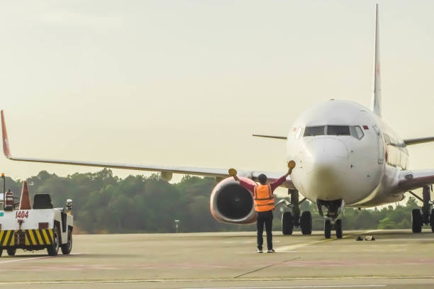 équipe au sol dans le gilet de signalisation. le commissaire de l’aviation ou le superviseur rencontre un avion de passagers à l’aéroport. l’avion roule jusqu’à la place de stationnement. agent de contrôle des mouvements de l’aire de trafic  - airport security staff photos et images de collection