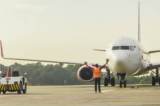 Batam, Indonesia - March 31, 2023: Ground Crew in the signal vest. Aviation Marshall or Supervisor meets passenger airplane at the airport. Aircraft is taxiing to the parking place. Apron movement control officer in safety vest parking
