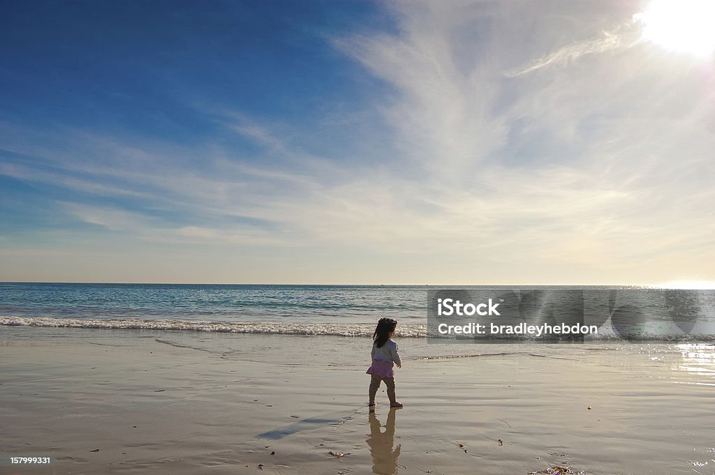 Baby Girl walks along a beautiful beach Ready to take on the world, an independent baby girl walks alone, along the wet sands of Laguna Beach in Southern California. A dramatic sky compliments the tranquil ocean. 12-17 Months Stock Photo