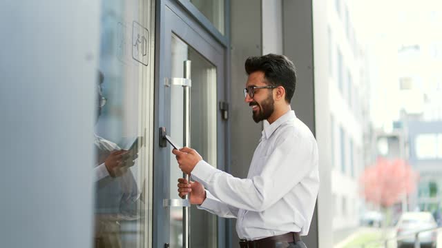 Young bearded businessman unlocking door using mobile phone application. Unlocks a modern office building
