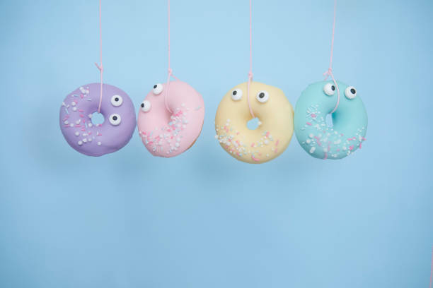 Four gourmet pastel donuts with googly eyes hanging on string on a blue background