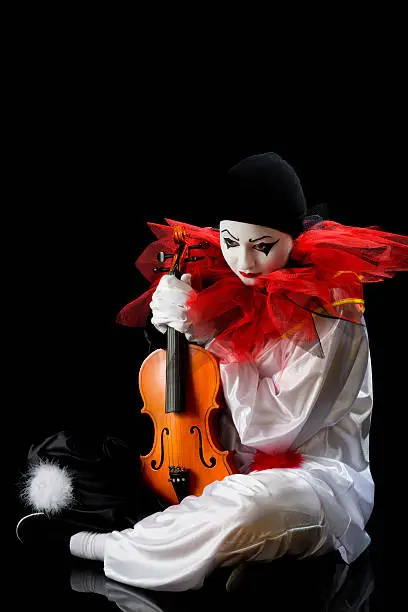 Sad Pierrot sitting on the floow with an old violin