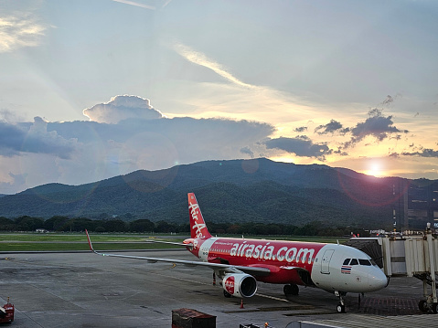 AirAsia planes dock and connect to jet bridge with sunset and mountains in the background. Taken on July 30, 2023, Chiang Mai, Thailand.