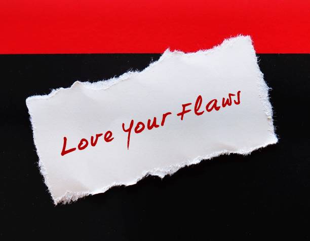 istock Torn note on red black background with handwritten text LOVE YOUR FLAWS, self talk to remind to learn self acceptance, embeace imperfection, learn to love yourself. 1580156447