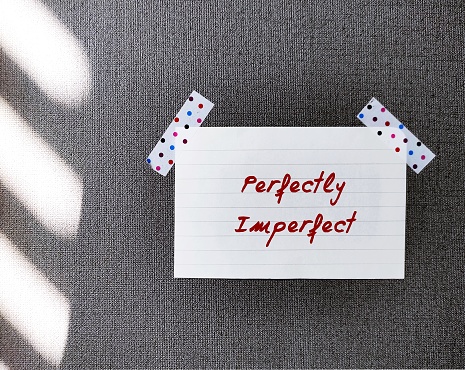 Stick note on wallpaper with handwritten text PERFECTLY IMPERFECT, concept of self acceptance, with all flaws, embracing imperfections which are often more valuable than perfections