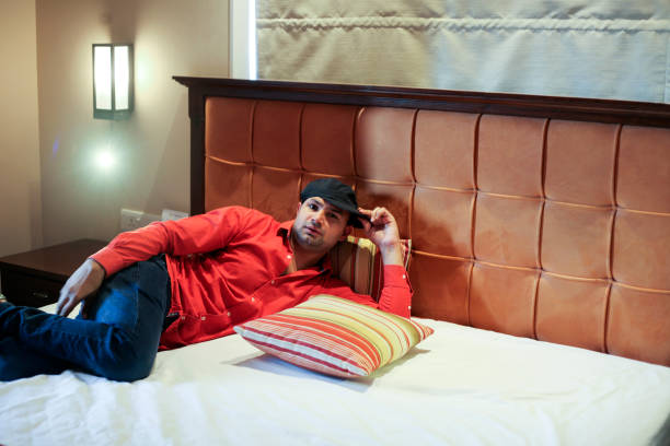 Young men of Indian ethnicity lying down on the bed in luxury hotel during vacation