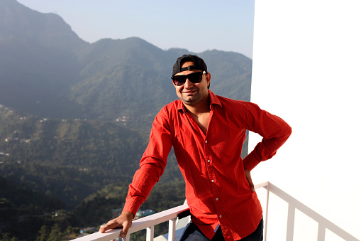 Confident young men of Indian ethnicity standing portrait in hotel balcony during vacation near mountain range in Shimla, Himachal Pradesh.