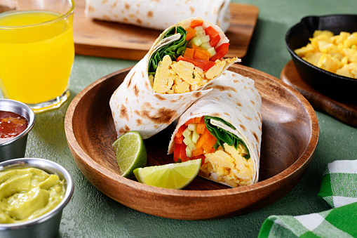 Homemade breakfast egg burrito with fresh vegetables and different sauces for healthy vegetarian breakfast.