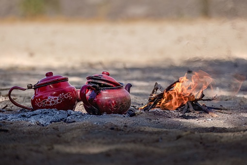 Two red teapots are sitting atop some rocks in front of a burning fireplace, creating a cozy and inviting atmosphere