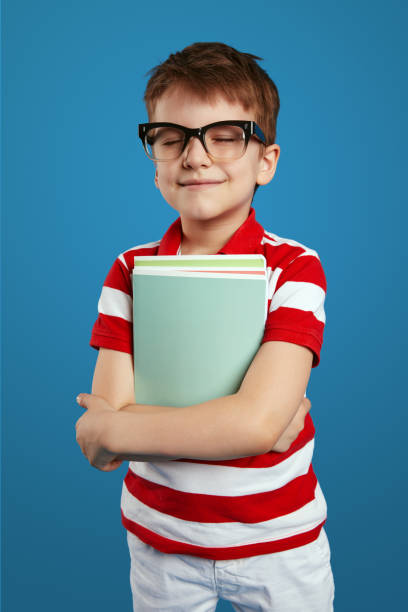 istock Delighted schoolboy in nerdy eyeglasses smiling and holding textbooks while standing with closed eyes 1580382081