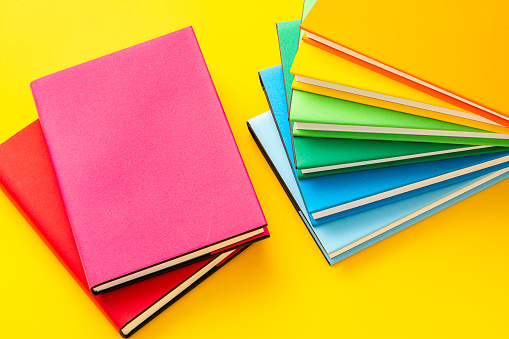 Raibow colored text books shot from above on yellow background.