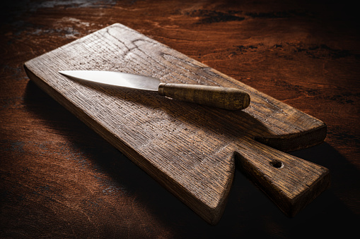 Wooden cutting board or chopping board and kitchen knife on rustic wood table low key kitchenware