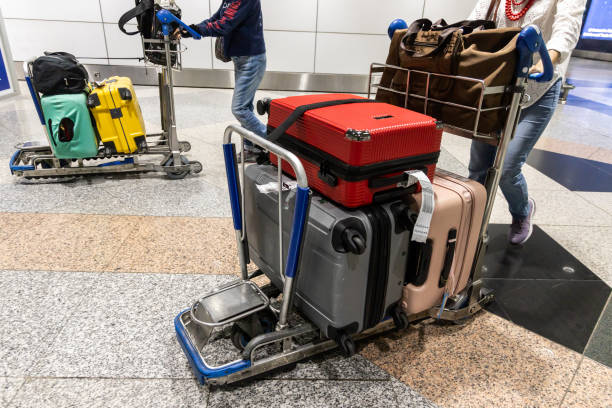 Luggage carts loaded with colorful suitcases being pushed through an airport terminal.