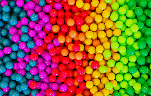 Rainbow colored balls or balloons in a huge pile. They are shiny and reflect the light.