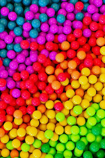 Rainbow colored balls or balloons in a huge pile. They are shiny and reflect the light.