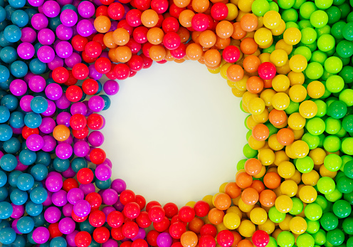 Rainbow colored balls or balloons in a huge pile with a hole in the middle. They are shiny and reflect the light.