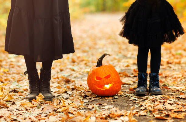 istock Mother and daughter standing outside with scary face pumpkin lantern between them 1580676971