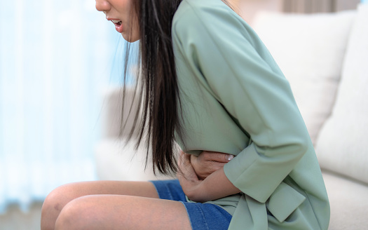 Asian woman suffering from severe abdominal pain, Acid reflux, Gastritis, Food poisoning, Appendicitis, Menstrual pain.