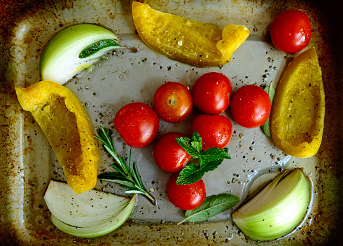 Raw, uncooked red tomatoes, yellow sweet peppers and sliced white onion on baking tray ready to be roasted or cooked with olive oil and fresh herbs. Healthy lifestyle vegan vegatarian dies and lifestyle.